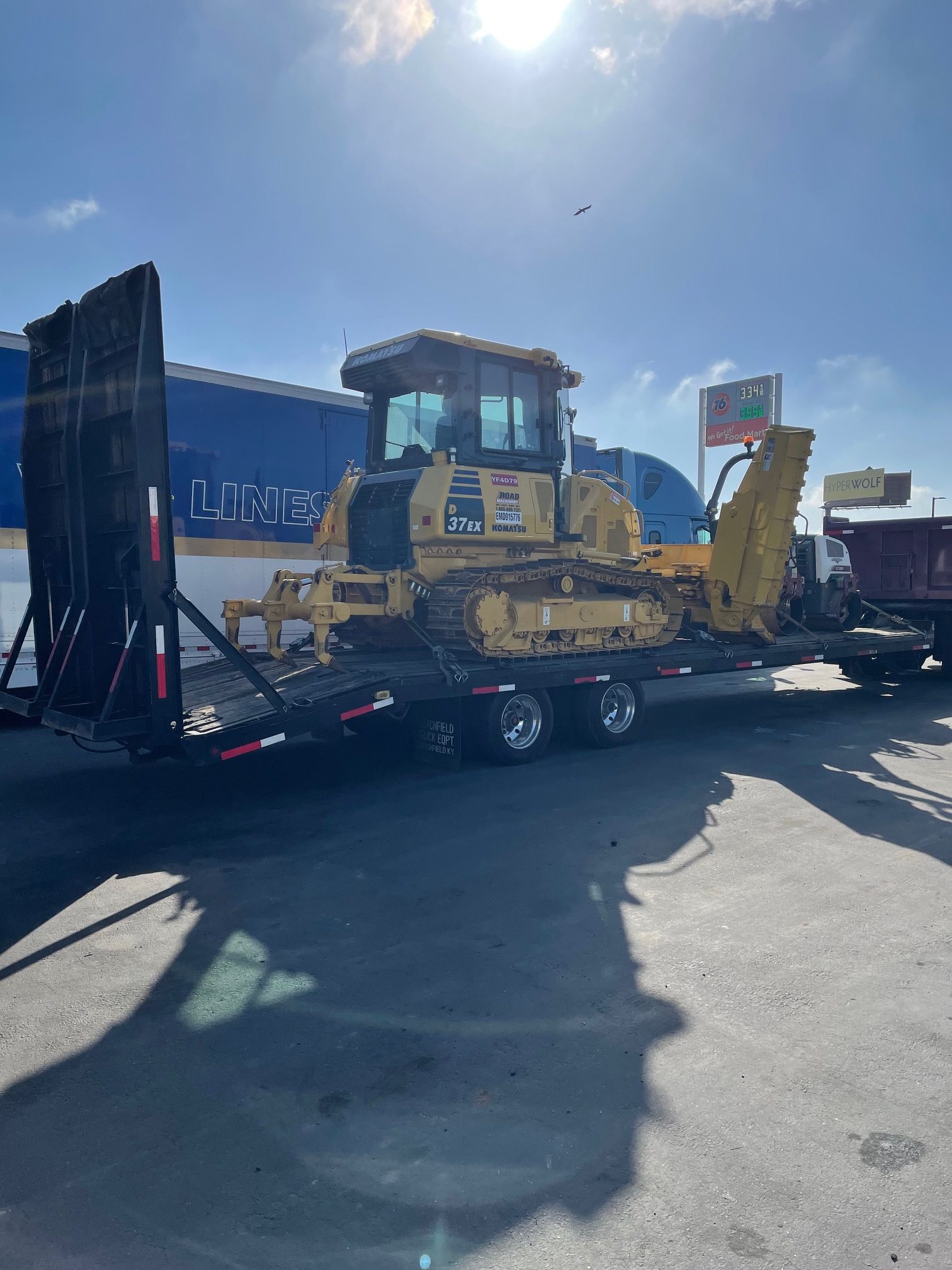 Heavy duty grading equipment and Komatsu bulldozer on a trailer flatbed, ready for an asphalt paving job by Black Diamond Asphalt SoCal.