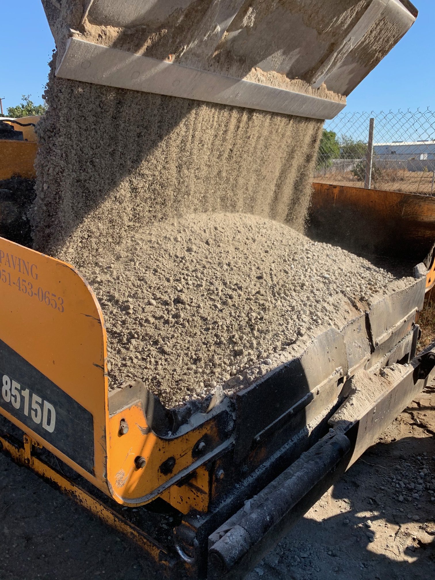 Heavy paving machinery pouring crushed aggregate base material for an asphalt paving project by Black Diamond Asphalt SoCal.